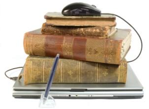 Photograph of laptop with old books and computer mouse on top representing old and new